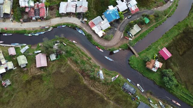 Cinematic drone view of a remote community at Laguna de la Cocha, Colombia, with boats, wooden docks and homes built along the lagoon in a natural setting.