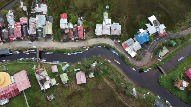 op-down aerial drone video of Laguna de la Cocha, showing a rural settlement, curved road and boats docked along the lagoon in southern Colombia.