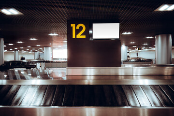 Airport baggage claim hall with conveyor belt and large pillar sign showing number 12 and blank...