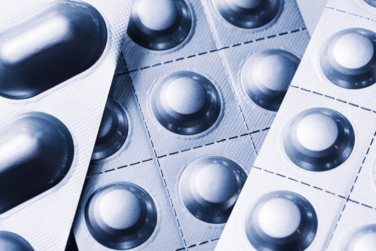 Blister packs with round tablets and capsules closeup. Pharmaceutical medicine packaging pattern. Sealed pills in aluminum foil sheets. Medical drug production detail view.