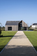 New building with wooden exterior sits on green landscape in a sunny day, surrounded by grass and trees, located in a serene area with clear sky and no clouds