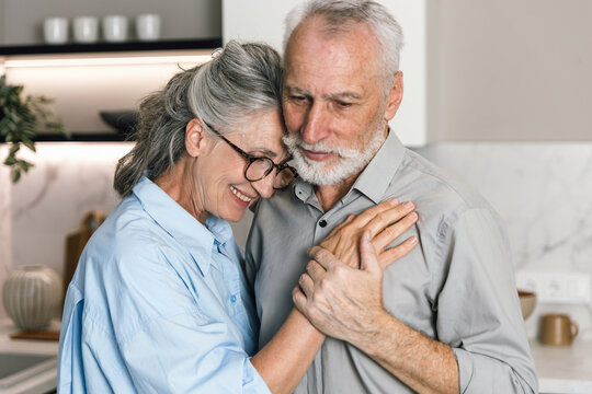 Senior couple smiles and embraces in their cozy home during the weekend