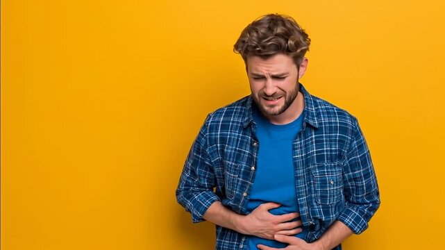 Casual man holding stomach feeling discomfort on yellow backgroundhd4k,HD4K,Male model showing digestive problem with hands,Young man experiencing stomach pain,Man feeling stomach ache