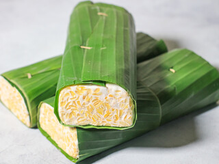 Tempeh wrapped in banana leaves with a marble background. Tempeh is a traditional Indonesian food made from soybeans. It is beneficial for health.