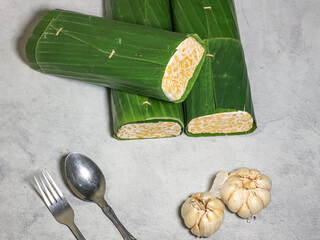 Tempeh wrapped in banana leaves with a marble background. Tempeh is a traditional Indonesian food made from soybeans. It is beneficial for health.