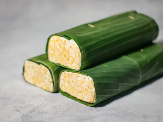 Tempeh wrapped in banana leaves with a marble background. Tempeh is a traditional Indonesian food made from soybeans. It is beneficial for health.