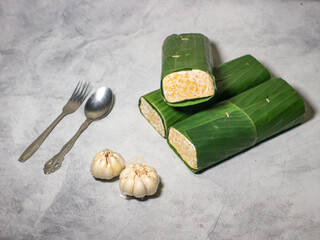 Tempeh wrapped in banana leaves with a marble background. Tempeh is a traditional Indonesian food made from soybeans. It is beneficial for health.