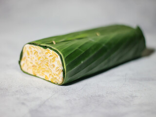 Tempeh wrapped in banana leaves with a marble background. Tempeh is a traditional Indonesian food made from soybeans. It is beneficial for health.