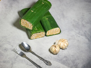 Tempeh wrapped in banana leaves with a marble background. Tempeh is a traditional Indonesian food made from soybeans. It is beneficial for health.