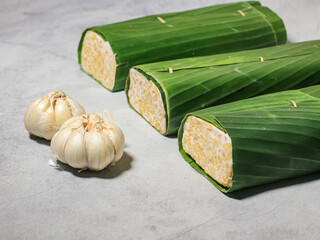 Tempeh wrapped in banana leaves with a marble background. Tempeh is a traditional Indonesian food made from soybeans. It is beneficial for health.
