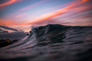 Fototapeta premium A breaking ocean wave at sunset at Bronte Beach, Sydney, Australia, with soft pink clouds and fading light reflecting across the water.