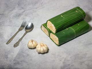 Tempeh wrapped in banana leaves with a marble background. Tempeh is a traditional Indonesian food made from soybeans. It is beneficial for health.