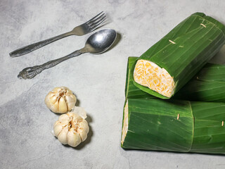 Tempeh wrapped in banana leaves with a marble background. Tempeh is a traditional Indonesian food made from soybeans. It is beneficial for health.