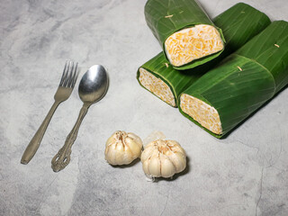 Tempeh wrapped in banana leaves with a marble background. Tempeh is a traditional Indonesian food made from soybeans. It is beneficial for health.