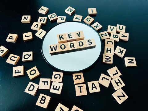 High-angle view of wooden letter tiles spelling "KEY WORDS" on a round mirror surrounded by scattered alphabet blocks on a black background.