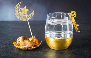 A glass of water with a Ramadan charm and dates with a crescent moon and star topper.