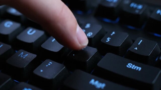 Close-up of a finger pressing a keyboard key, with illuminated blue details