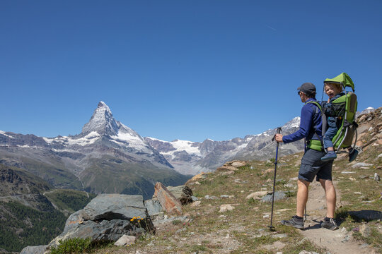 father hikes with child in carrier backpack, Zermatt, Switzerland