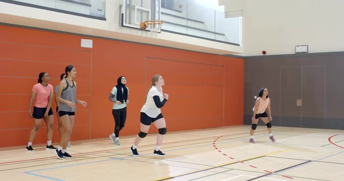 Serve hitting gym sending White player running under hoop in kneepads bumping volleyball for rally
