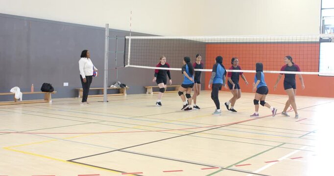 African American coach giving high-fives to blue-jersey team at gym net showing respect, copy space