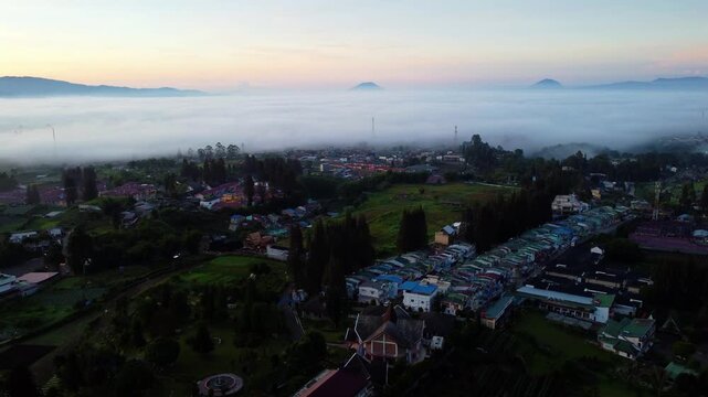 Aerial view of Berastagi town shrouded in thick morning mist and fog with mountain landscape, North Sumatra, Indonesia