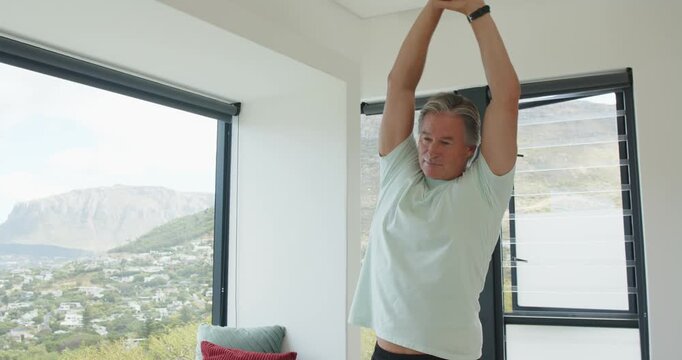 Mature male raising arms bending rolling wrists warming at home by windows, smartwatch, copy space