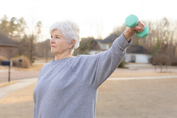 Senior woman exercising with dumbbells outdoors from side angle