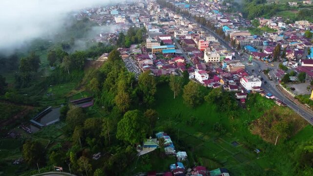 Aerial view of Berastagi town shrouded in thick morning mist and fog with mountain landscape, North Sumatra, Indonesia