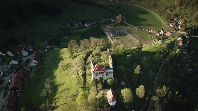 Smooth 4K UHD drone pull-back (reverse dolly out) retreating from Burgruine Niedergundelfingen on the Schlo&szlig;berg in M&uuml;nsingen-Gundelfingen, revealing nearby village houses, fields, and the Gro&szlig;e Laute