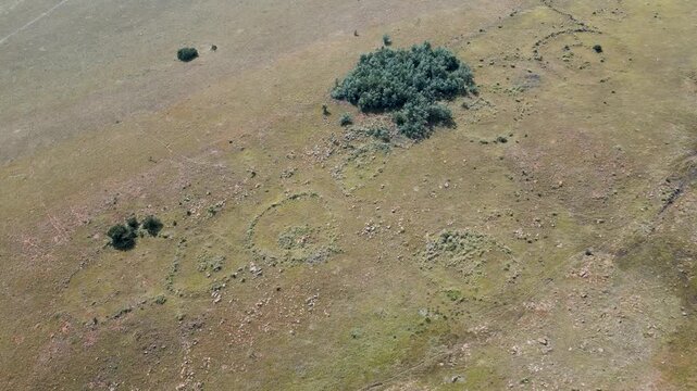 Drone shot passing over rural South African farmland and ancient circular stone kraals traditional livestock enclosures