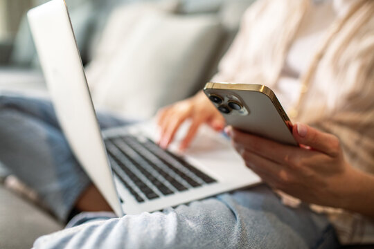 Person using smartphone and laptop on sofa at home