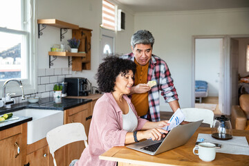 Obraz premium Middle-aged couple reviewing bills on laptop at kitchen table