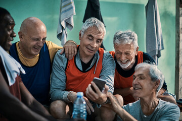 Senior men teammates laughing at smartphone in locker room