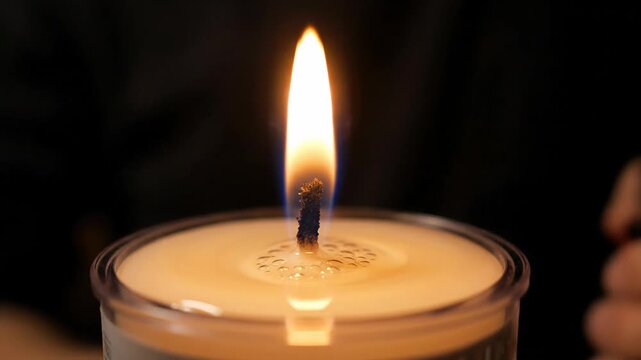 Close-up of a hand lighting a candle wick with a lighter, flame igniting slowly
