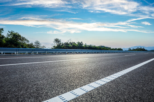 Empty asphalt highway with white lines and metal guardrails under a blue sky with white clouds