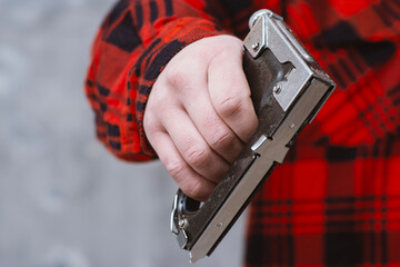 Close up of male hand in red checkered work shirt holding black manual staple gun against neutral gray background. Concepts of construction and DIY home renovation.