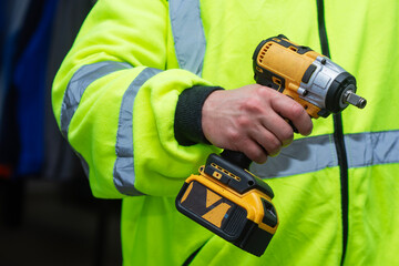 Construction worker in high visibility safety jacket holding professional cordless impact wrench power tool.