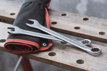 Two metal wrenches on a red tool bag lying on a perforated wooden workbench in a workshop. Concepts of mechanical repair and automotive service.
