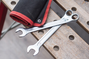 Two metal wrenches on a red tool bag lying on a perforated wooden workbench in a workshop. Concepts of mechanical repair and automotive service.