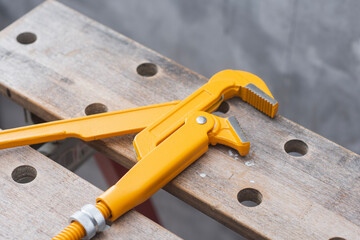Professional yellow adjustable pipe wrench lying on wooden workbench in workshop for plumbing repair work.