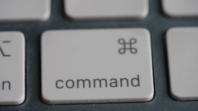 Extreme close up of a finger pressing the command key on a white chiclet style keyboard. Ideal for technology, software development, and shortcut tutorials.