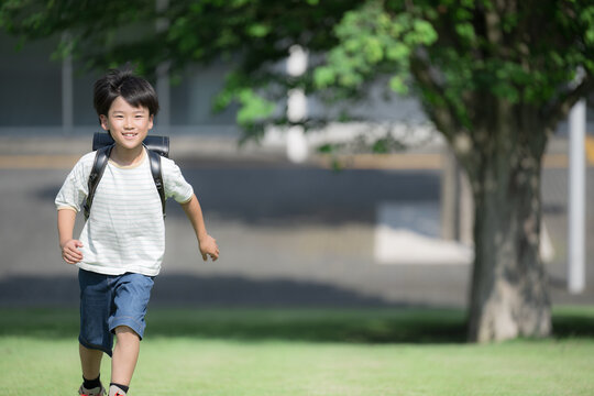 学校の校舎を背景に校庭でランドセルを背負って走る少年の(男の子)男子のカメラ目線の笑顔　右にコピースぺースありの全身