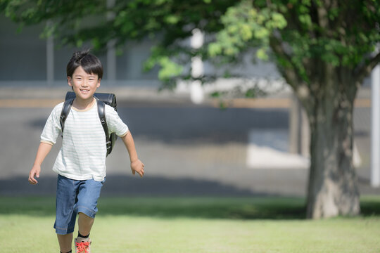 学校の校舎を背景に校庭でランドセルを背負って走る少年の(男の子)男子のカメラ目線の笑顔　右にコピースぺースありの全身