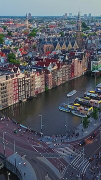 Aerial View of Traditional Dancing Houses Along Damrak Canal, St. Nicholas Basilica, and Busy City Traffic at Dusk in Amsterdam