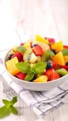 A vibrant close-up showcases a bowl filled with a colorful mix of freshly cut fruits and leafy green garnish, resting on a patterned cloth