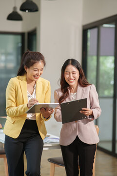 Two Asian businesswomen working with documents in an office.