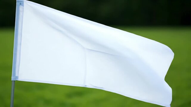 A single white flag waving gently in the breeze against a soft-focus green background, symbolizing peace, truce, or surrender