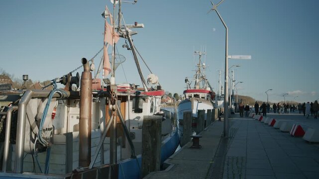Fishing boats moored along a harbor pier in Eckernf&ouml;rde. Calm water, maritime equipment and a promenade with people create a relaxed coastal harbor scene in daylight.