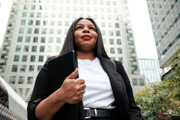 Businesswoman walking in financial district holding tablet and looking up