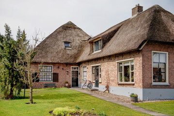 Obraz premium Giethoorn, Netherlands, April 08 2018: A charming traditional thatched-roof house surrounded by lush greenery in Giethoorn